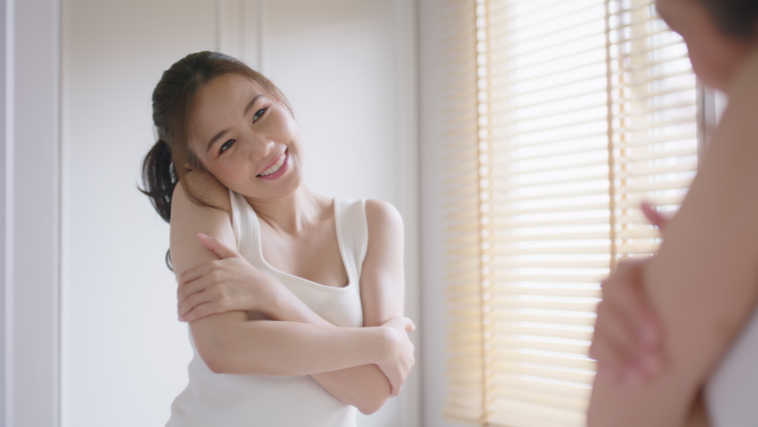 Young adult asia people woman hug love arm around believe trust smile look at mirror in body skin care. Single asian lady girl self esteem talk pride proud of myself life in morning fresh at cozy home Royalty-Free Stock Footage #1096251473