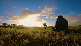 Man photographer with camera on gimbal shooting fascinating time lapse near railway with clouds in sky sunset. Day to night. Beautiful fairy landscape in fast motion