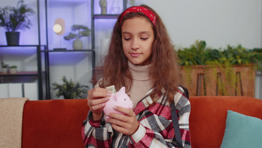 Poor young preteen girl child kid insufficient amount of money, holding piggybank and one dollar banknote at home. Financial crisis. Bankruptcy. Poverty and destitution. Teenager children at home room