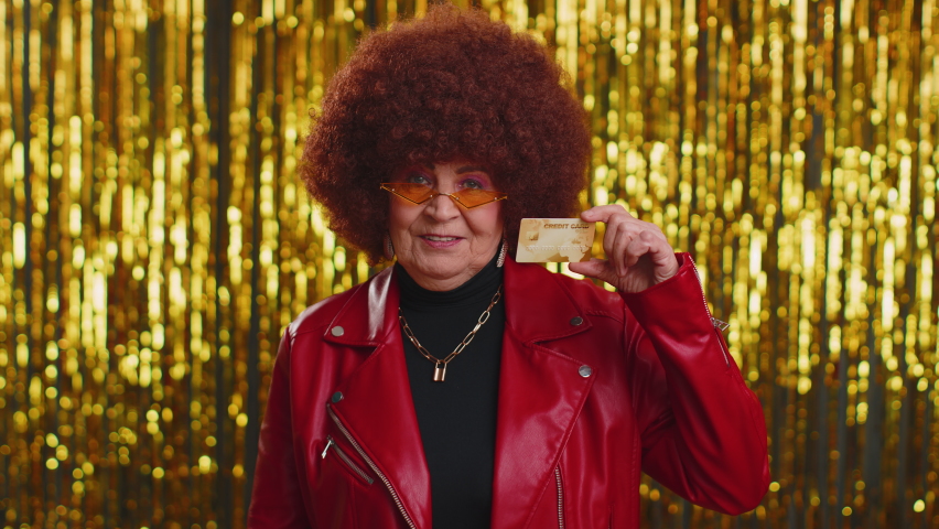 Happy woman showing plastic credit bank card advertising transferring money cashless, purchases online shopping, sale discount, internet order delivery purchase. Senior grandmother on shiny background