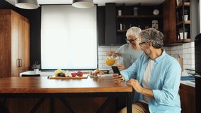 Senior woman pouring orange juice and talking to her husband in the kitchen. - Powered by Shutterstock - Get 15% off with code: PIKWIZARD15