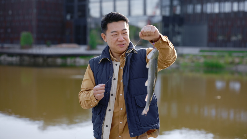 Portrait asian male feeling happy because he caught a fish and keeps it on the hook and looking at the camera smiling. People and fishing concept