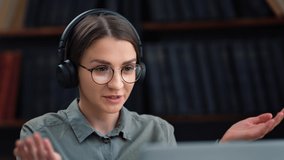 Smiling beauty brunette female in headphones talking online video call use laptop web camera working at library home office. Happy cute woman remotely communication e learning academic education