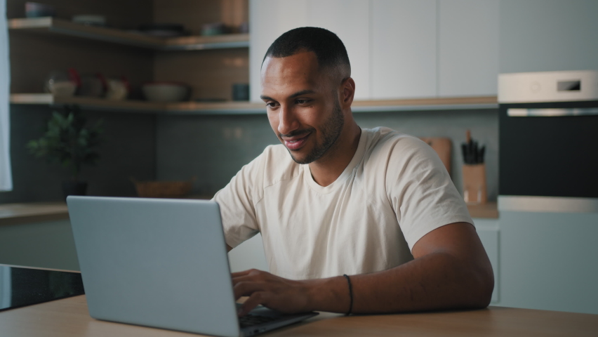 Smiling African millennial man guy American male user freelancer at home kitchen finish distant work with laptop satisfied with computer app online website networking shopping looking at camera smile Royalty-Free Stock Footage #1096268443