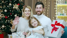 Cheerful family parents and little girl kid child greeting remotely video conferencing chat call online talk congratulations Merry Christmas Happy New Year winter holidays looks at camera webcam view