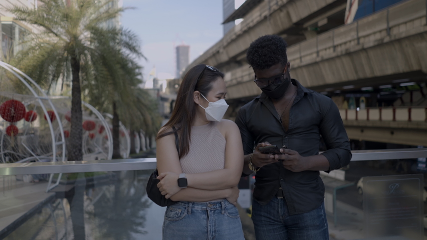 Mixed race couple go on a date in the city of Bangkok. They wear face masks and walk around huge hall 