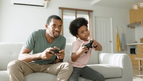 African American Father and his Little son sitting on couch using game controllers playing console video game