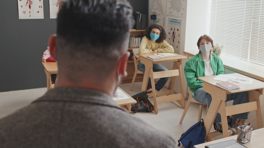 Rear view of male professor giving anatomy lecture to young students who wearing face masks and sitting at desks in morning - Powered by Shutterstock - Get 15% off with code: PIKWIZARD15