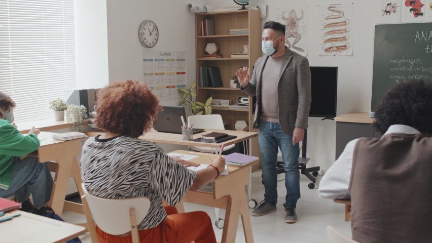 Wide shot of male Caucasian professor wearing face mask, giving anatomy lecture to young students who sitting at desks in morning - Powered by Shutterstock - Get 15% off with code: PIKWIZARD15