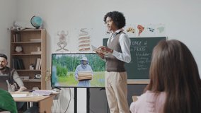 Medium long low angle of Black guy making presentation to classmates, showing educational video about bees