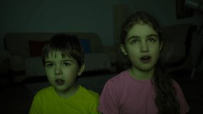 Brother and Sister Watching TV, Eating Popcorn Sitting on Floor at Home. Two Children Watching Exciting Movie in Living Room. Portrait Little Kids While Watch TV. Children Watch Television at Evening.