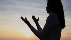 lifestyle slow motion video of Silhuette Young Woman praying on the mountain at sunrise.  prayer,  Girl  hands in prayer pray to God. the girl praying asks forgiveness for sins.