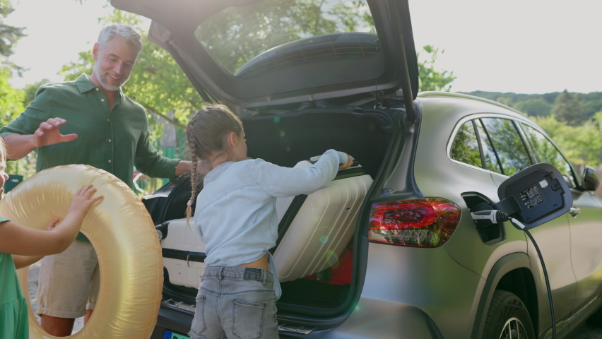 Father with kids packing suitcases into electric car trunk while charging battery. Royalty-Free Stock Footage #1096285721