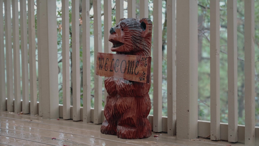 A static footage of a wooden bear sculpture holding a welcome sign