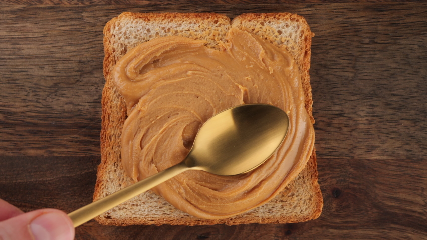 Peanut Butter Spreading on bread with a golden spoon, top view. Perfect traditional breakfast Royalty-Free Stock Footage #1096289045