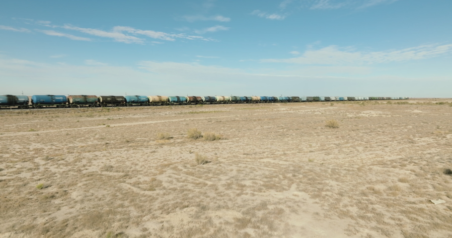 Freight long train carries with oil tank and petrol carriages an locomotive by arid flat plain steppe. Railways in wild desert. Aerial drone perspective view at summer sunset Royalty-Free Stock Footage #1096291697