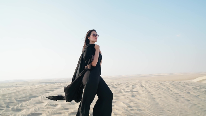 Young beautiful girl in traditional Abaya dress stand along the dunes in the desert of Qatar
