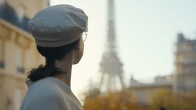 Portrait of a young female tourist in a cap looking at the Eiffel Tower