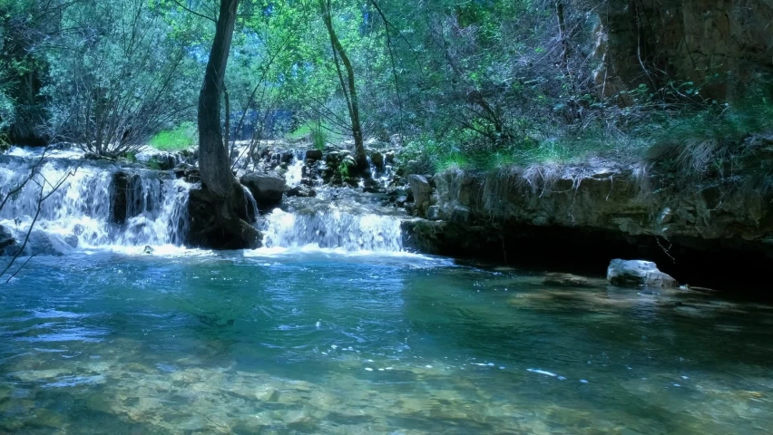 Beautiful fairy waterfall at wild forest. Fresh water waterfalls river flowing. Forest rocks with a roaring stream running. Lush foliage.Panoramic landscape of green nature. Rocks, stones, trees.