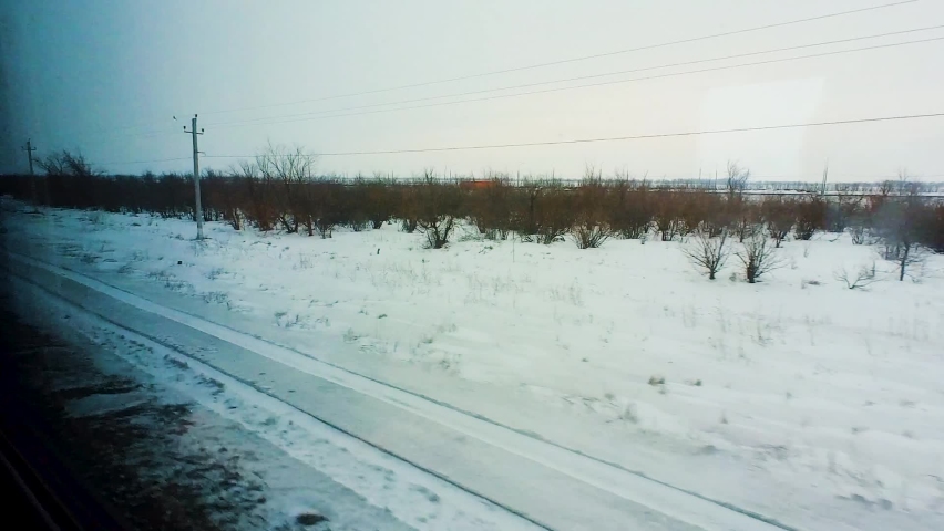 Winter snow-covered landscape is visible from the window of a passing train. Winter travel
