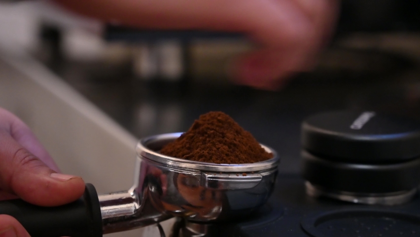 Barista hand holding and pressing tamper on coffee grounds powder in portafilter ready to make cup of coffee