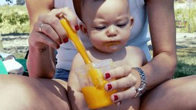 mom feeding an orange vegetable puree to her baby in the field with a silicone spoon, baby care and nutrition concept, 4k video, medium shot, slow motion