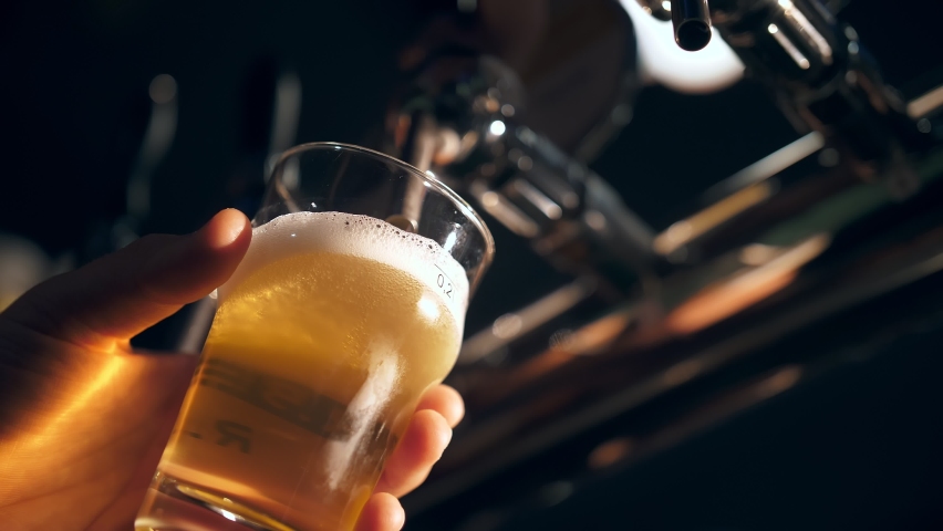 The bartender pours beer into a glass. Close-up view of barman's hand filling glass with light beer, at bar table, at pub. Pouring beer into mug, at beer bar Royalty-Free Stock Footage #1096312797