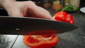 Slow motion close-up video of cutting a red bell pepper with a knife. Preparing a salad in the kitchen with a cupboard. High quality 4k footage