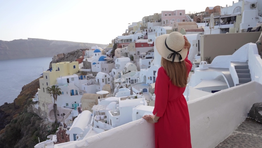 Fashion traveler girl in Oia picturesque greek village of Santorini Island. Young woman enjoying holidays in Greece, Europe.