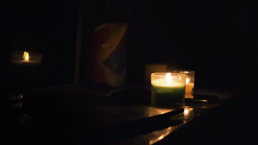 Burning candles, laptop and cellphone on the table. Candles in dark room. No electricity in the house. Power outage in the city. Blackout, energy crisis concept.  Royalty-Free Stock Footage #1096329073