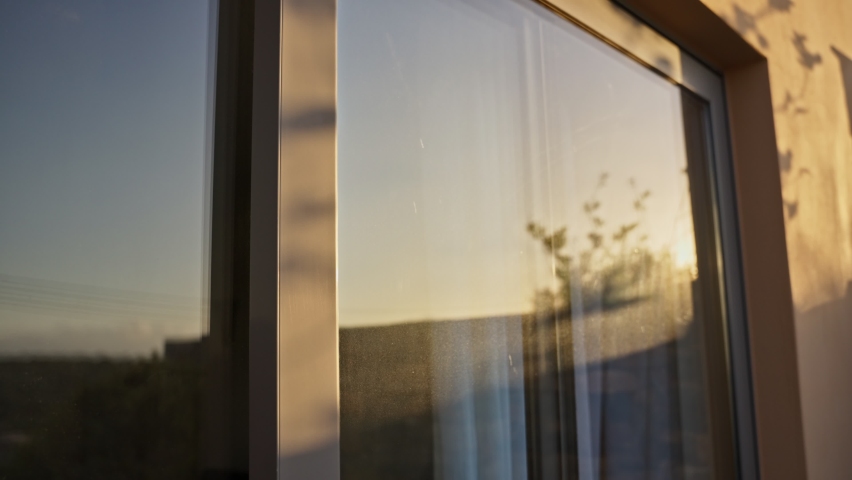 Sunset or sunrise as sun reflects on dusty windows or glass doors of house. Flare hits the glass as sun is setting or rising in early morning or sundown. Hot day. Green solutions for solar energy | Shutterstock HD Video #1096331589