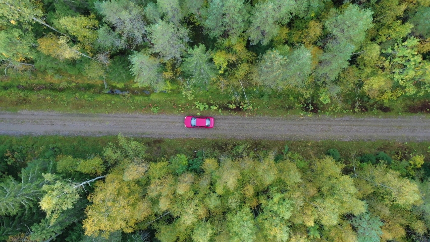 A red car driving in the colorful forest in the autumn filmed with a bird's eye view. The drone overhead shot was filmed in a typical Scandinavian forest in the fall in Finland. Royalty-Free Stock Footage #1096332209