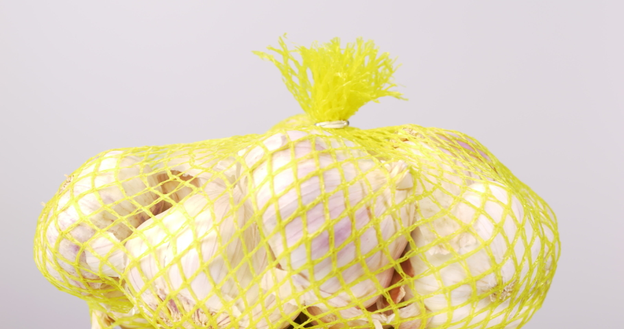Close-up of large cloves of garlic gathered in mesh bags on a table.
