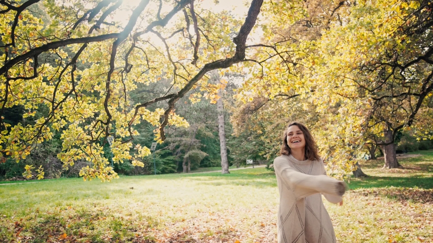 Cinematic slow-motion footage. A young adult caucasian woman having fun and enjoying the sunny weather at the autumn park.