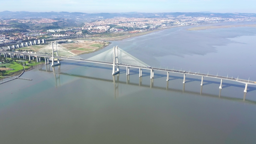 Cinematic aerial view of Vasco da Gama Bridge. Is a cable-stayed bridge flanked by viaducts that spans the Tagus River in Lisbon. It is the second longest bridge in Europe. Drone backward 