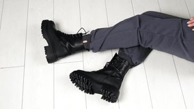 Presentation of black leather stylish army boots with laces. Modern sitting on the floor showing her modern footwear on tractor soles.