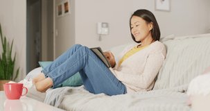 Video of happy asian woman resting on sofa with tablet. Leisure, relax, spending time at home with technology concept.