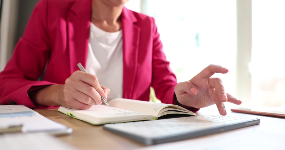 Businesswoman working on computer using typing corporate message and writing notes in notepad