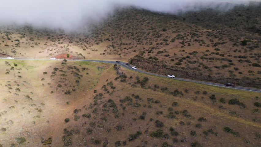 Tourists drive up Haleakala volcano through clouds toward the national park on winding mountain road
