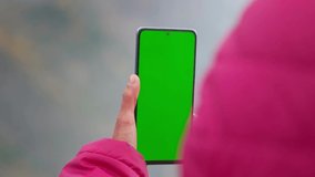 Closeup shot of Indian girl wearing jacket and using mobile phone with Green screen. Green screen mockup template of Mobile phone, Chroma key.  Finger swiping up in green screen of the mobile