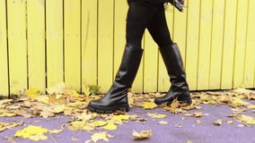 A girl in warm boots poses against a background of fallen foliage