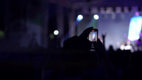 Silhouette of a man on rock concert filming guitarist on the stage by the smartphone in his hands. Crowd is dancing in the darkness in front of band at open air music performance. Entertainment theme.