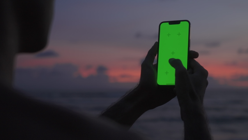 Silhouette man holds vertical mobile phone one hand and swiping touch screen. Use green screen for copy space closeup. Chroma key mock-up on smartphone. Film pixel grain texture.  | Shutterstock HD Video #1096371801