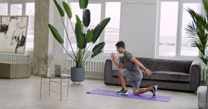 Athletic fitness coach in sportswear doing lunges exercise at home while providing online lesson via laptop