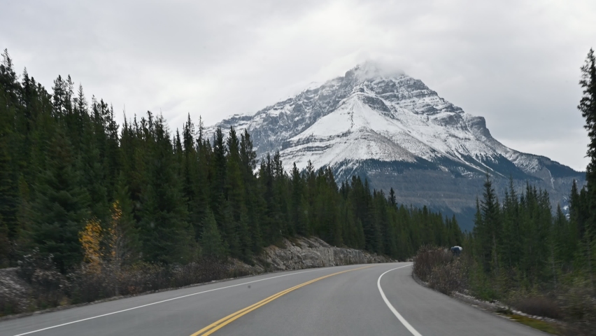 Road trip of car driving on highway with Rocky mountains and pine forest on overcast day in Banff national park at Alberta, Canada