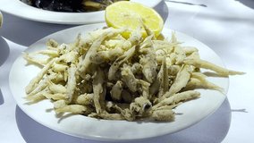 Sun shining on Deep Fried Smelt Fish, high angle view. Stack of seafood served with half a lemon piece. Delicious crispy Atherina. Mediterranean food background video in 4k resolution, copy space.
