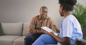 4K video footage of a Female professional doctor consulting senior patient during medical care visit. Young woman physician and old man talking providing medical assistance sitting on sofa. 