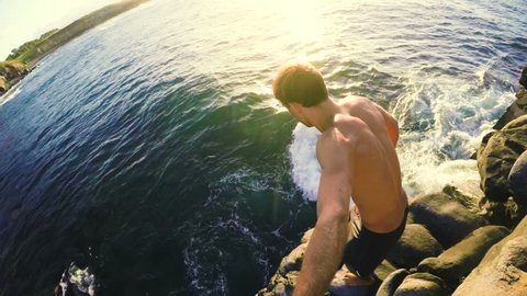 GOPRO POV of Athletic Young Man Jumping from Sea Cliffs into the Blue Ocean in Hawaii at Sunset.