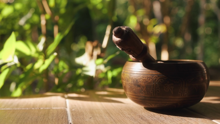 Metal sound bowl on wooden floor with tropical vegetation in the background and side lighting during golden hour in Tulum Royalty-Free Stock Footage #1096383165