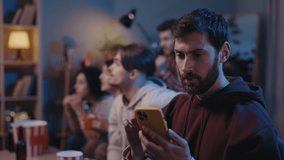 Positive bearded cheerful man looking at his smartphone with happy emotions during football game. Handsome unshaven male fan using modern smartphone on at home. Football fans concept - Powered by Shutterstock - Get 15% off with code: PIKWIZARD15